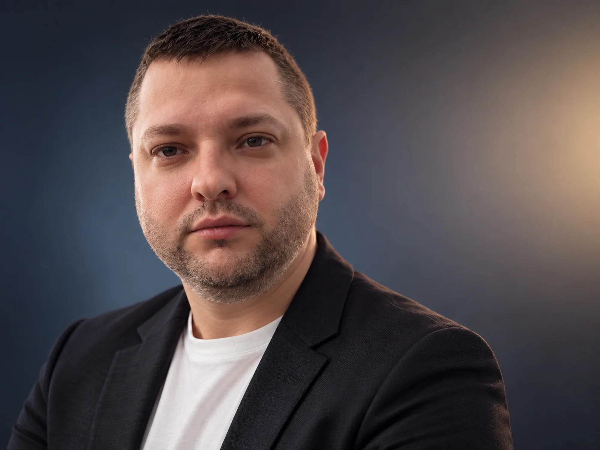 Alexey in a dark blazer and white shirt against a dark blue background